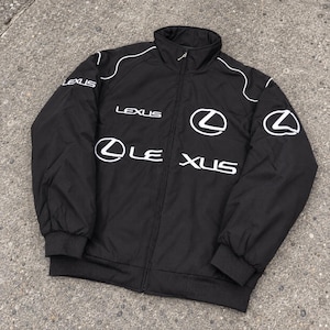 May include: A black zip-up jacket featuring white Lexus branding and logos printed on the chest, sleeves, and shoulders. The jacket has a high collar, long sleeves with ribbed cuffs, and a full-length front zip closure with a silver pull tab.