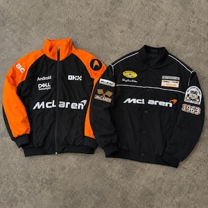 Può includere: Due giacche da corsa McLaren nere. Una giacca ha dettagli arancioni, il logo McLaren e la scritta "Android Dell Technologies". L'altra giacca è nera con dettagli bianchi, il logo McLaren e la scritta "1963".
