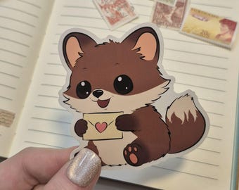 May include: A sticker featuring a cartoon fox holding a small envelope with a heart. The fox is brown and white with large black eyes. The sticker is held in front of an open notebook with stamps.
