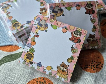 May include: A stack of square sticky note pads featuring a light pink and white checkered border. The border is decorated with illustrations of small animals, including raccoons and mice, interacting with various fruits like pineapples, peaches, and blueberries, along with small jars of juice.