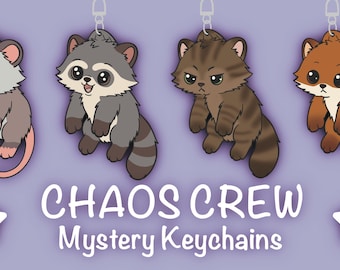 May include: Four cartoon animal keychains: a gray opossum, a gray raccoon, a brown cat, and a brown fox. The keychains are suspended from silver chains. The text "CHAOS CREW Mystery Keychains" is displayed below the keychains on a purple background.