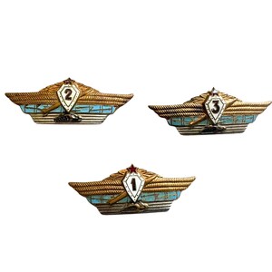May include: Three vintage military badges with a wing design. Each badge features a central shield with a number (1, 2, or 3) and a red star. The wings are gold-toned with blue and white accents.