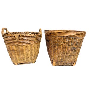 May include: Two brown woven baskets with a tapered shape and square base. The left basket features two integrated side handles, while the right basket has a smooth, continuous rim. Both items are constructed from thin, flexible strips of wood.