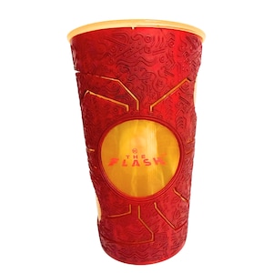 Può includere: Un bicchiere di plastica rosso con una superficie strutturata con intricati motivi geometrici e un emblema circolare giallo centrale. Il testo THE FLASH è stampato in rosso all'interno del cerchio giallo e ha un bordo giallo chiaro.