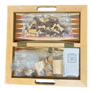 May include: A wooden folding game board featuring a backgammon layout with light and dark wood triangles. Inside are two clear plastic bags containing dark and light wooden chess pieces, round checkers, two wooden dice cups, and a printed instruction manual.