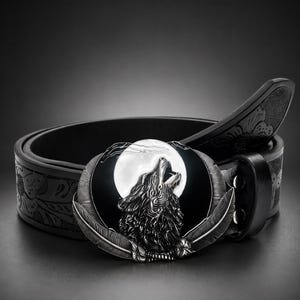 Peut inclure: Une ceinture en cuir noir avec une boucle ovale en métal représentant un loup argenté hurlant à la lune blanche. La boucle est encadrée par deux plumes argentées détaillées à la base. La sangle de la ceinture présente un motif floral en relief.