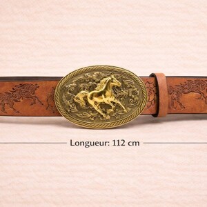 May include: Brown leather belt with a gold-colored oval buckle featuring a horse design. The belt has embossed horse and floral patterns. The belt measures 44 inches in length.