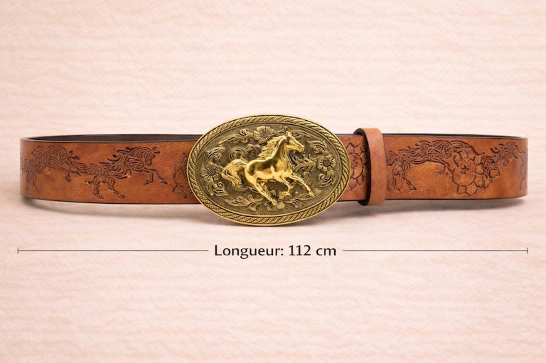 May include: Brown leather belt with a gold-colored oval buckle featuring a horse design. The belt has embossed horse and floral patterns. The belt measures 44 inches in length.