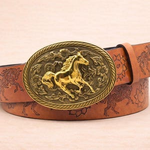 May include: A brown leather belt with a gold-colored oval buckle featuring a horse design. The belt has a floral and horse pattern. The buckle is approximately 3 inches wide and 2 inches tall.