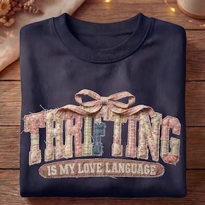 May include: Navy blue sweatshirt with the word "THRIFTING" in a patchwork design, topped with a bow. The phrase "IS MY LOVE LANGUAGE" is below the word "THRIFTING".
