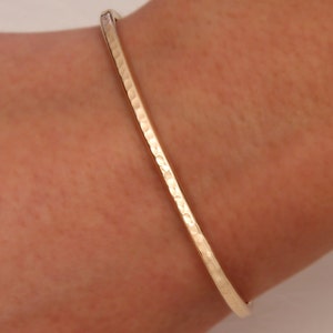 May include: A gold hammered bangle bracelet. The bracelet is simple and elegant, with a smooth, polished finish.