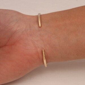 May include: A gold hammered cuff bracelet with a simple, minimalist design. The bracelet is open and adjustable to fit most wrists.