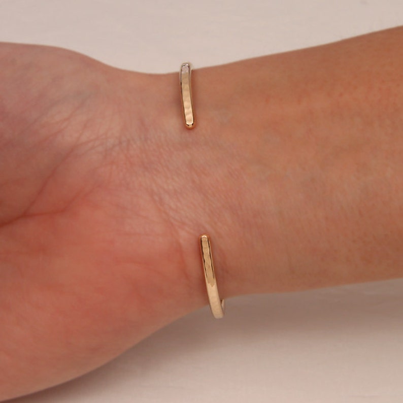 May include: A gold hammered cuff bracelet with a simple, minimalist design. The bracelet is open and adjustable to fit most wrists.