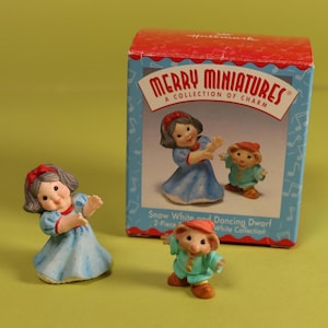 May include: A collection of Hallmark Merry Miniatures figurines. The set includes a Snow White figurine in a blue dress with a red bow, and a dancing dwarf figurine in a green outfit. The box reads "Merry Miniatures, A Collection of Charm."