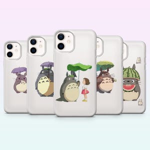 Puede incluir: Cinco fundas transparentes para teléfono con ilustraciones de personajes de Totoro. Cada funda presenta un diseño diferente, incluyendo a Totoro con un paraguas, una niña y un sombrero de sandía. Las fundas se muestran sobre un fondo degradado.