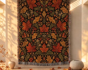 May include: A woven throw blanket featuring a repeating botanical pattern of red maple leaves, brown acorns, green oak leaves, and small white flowers on a black background, finished with a fringed edge along the top and bottom borders.