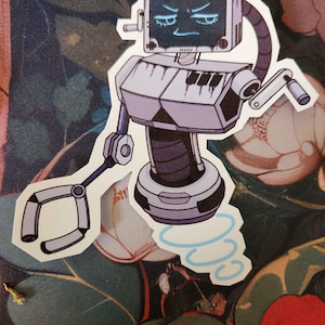 May include: A sticker featuring a robot character with a screen face displaying an angry expression. The robot has a keyboard chest, articulated arms, and a swirling blue design at its base. The color palette includes shades of gray, black, and blue.