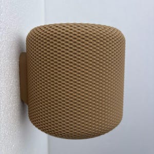 Pode incluir: Um objeto cilíndrico bege, montado na parede, com um padrão texturizado semelhante a tecido. O objeto é fixado à parede com um pequeno suporte retangular da mesma cor. O design é moderno e minimalista.