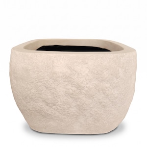 Puede incluir: Una maceta cuadrada con una superficie exterior rugosa y texturizada en un acabado de color beige claro similar a la piedra. La maceta presenta un borde ancho y liso que da paso a un cuerpo irregular, con una cavidad interior oscura.
