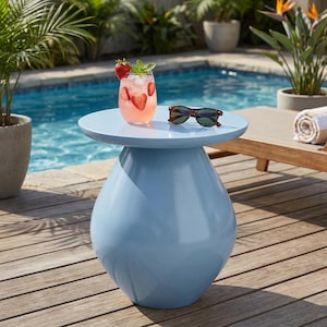 May include: A light blue outdoor side table with a round top and a bulbous base. A cocktail with strawberries and sunglasses rest on the table. The table is next to a pool and wooden deck.