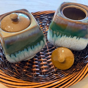 May include: A white ceramic mug with a black handle and the text "But First, Coffee" in a bold, black font. The mug is set against a blurred background, highlighting its clean design.