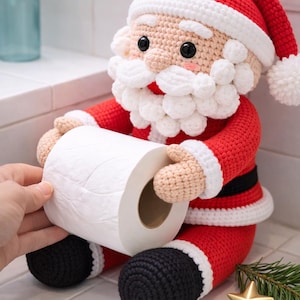 May include: A crocheted Santa Claus figure featuring a red suit with a black belt, white trim, and a matching red hat with a white pom-pom. The figure has a textured white beard and holds a standard roll of white toilet paper in its hands.