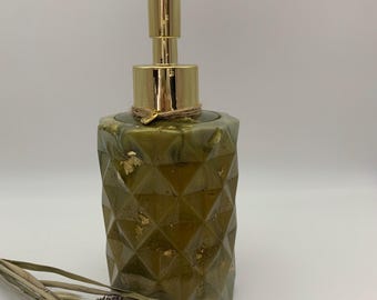 Moderno dispenser di sapone color verde oliva con dettagli in foglia d'oro e testina di erogazione color oro.
