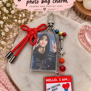 May include: A rectangular photo bag charm featuring a portrait of a person making a peace sign, a red cord bow, and a silver chain with colorful beads, a microphone charm, and a star. A second rectangular tag reads HELLO, I AM... KIM TAEHYUNG BIASED.