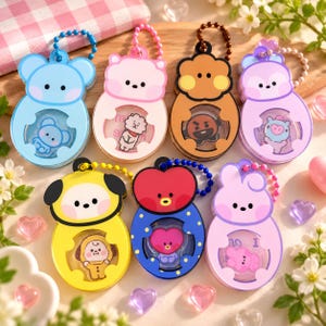 May include: Seven colorful character-themed plastic keychains with ball chains. Each keychain features a unique cartoon face and a clear circular window displaying a small character figure inside. The designs include blue, pink, brown, purple, and yellow.