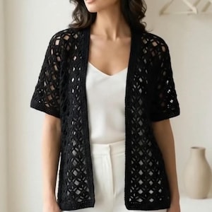Può includere: Un cardigan nero all'uncinetto, a maniche corte e aperto sul davanti. Presenta un motivo a rombi. Il cardigan è indossato sopra un top bianco e abbinato a pantaloni bianchi. Lo stile generale è casual ed elegante.