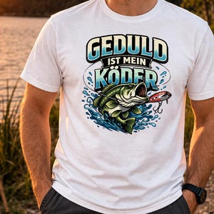Könnte beinhalten: Weißes T-Shirt mit einer Grafik eines aus dem Wasser springenden Fisches, einem Köder und dem Text "GEDULD IST MEIN KÖDER". Das Shirt wird von einer Person getragen, die sich in der Nähe eines Sees befindet.