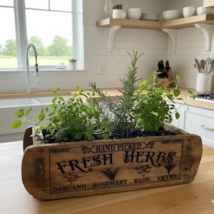 May include: A wooden planter box filled with fresh herbs, including rosemary and basil. The box is labeled "FRESH HERBS" with "Hand Picked" and herb names. The planter sits on a wooden countertop in a bright kitchen setting.