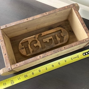 May include: A rectangular wooden mold with rusted metal edges and a carved wooden insert featuring Hindi script at the base. A yellow measuring tape is positioned along the front, showing the mold length is approximately 13.5 inches long.