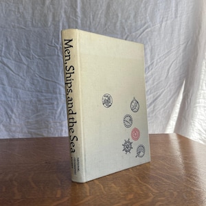 May include: A hardcover book titled Men, Ships, and the Sea by the National Geographic Society. The off-white cover features a vertical title and five small circular illustrations of nautical instruments in black and red ink.