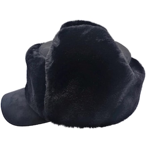 May include: A black trapper hat featuring a soft, dense faux fur exterior that covers the crown and ear flaps. The hat includes a smooth, matte-textured brim extending from the front, providing a contrast to the plush, fuzzy texture of the main body.