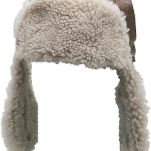 May include: A brown faux leather trapper hat featuring a thick, cream-coloured faux shearling lining on the front brim and ear flaps. The hat has a textured, weathered finish on the exterior and includes a black adjustable strap with a buckle.