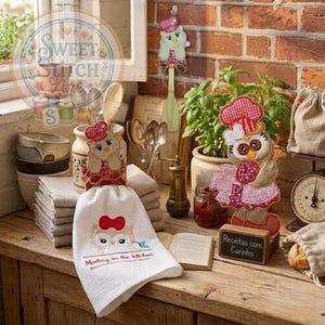 Puede incluir: Una exhibición temática de cocina con decoraciones de búhos. Incluye una toalla blanca con un diseño de búho y el texto "Meeting in the kitchen". Hay figuras de búhos y un adorno colgante, todos con gorros de chef.