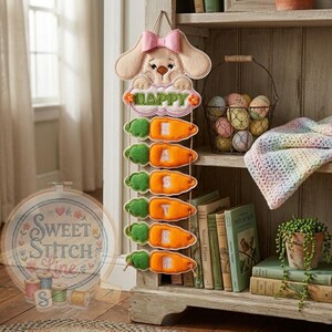 Pode incluir: Enfeite de parede de coelho da Páscoa em feltro com laço rosa, a palavra "HAPPY" e enfeites em forma de cenoura que soletram "EASTER". O coelho é bege e as cenouras são laranja e verde. Uma decoração charmosa.