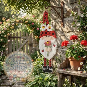 May include: A whimsical garden gnome decoration with a red hat covered in black spots, white beard, and holding a flower. The gnome is adorned with ladybugs and daisy accents, hanging from a metal bracket on a stone wall.