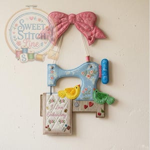 May include: A decorative wall hanging featuring a light blue sewing machine with floral accents, a pink bow, and two birds. The design includes the text "I Love Embroidery" on a small quilt, and a logo that says "Sweet Stitch Line".