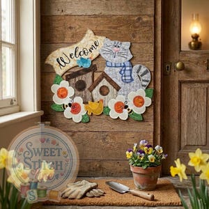 May include: A wooden welcome sign with a grey cat wearing a blue scarf, birdhouses, and floral details. The sign says "Welcome" and is decorated with flowers, bees, and birds. The sign is attached to a wooden door.