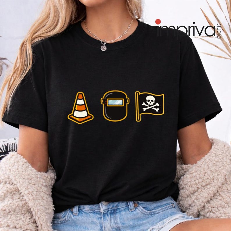 以下が含まれることがあります： 黒いTシャツ。交通コーン、溶接マスク、ドクロと骨の旗の3つのグラフィックアイコンが描かれています。アイコンは黒い線で縁取られ、オレンジ、黄色、白で塗りつぶされています。柔らかい素材で作られています。