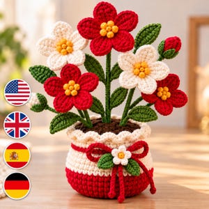 May include: A crocheted potted plant featuring vibrant red and white flowers with yellow centers, green leaves, and a small red bud. The pot is cream and red with a decorative red bow and a small white flower accent on the front.