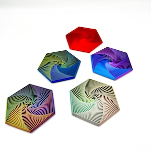 Puede incluir: Cinco posavasos hexagonales en varios colores: rojo, azul, morado, verde y un degradado arcoíris. Cada posavasos presenta un diseño en espiral, creando un efecto visual dinámico. Los posavasos están dispuestos sobre un fondo blanco.
