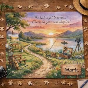 May include: A completed jigsaw puzzle depicting a lakeside scene with mountains and a sunset. The puzzle includes the text "The best is yet to come... Cheers to your next chapter!" and is personalised with the name "Mark". The puzzle is surrounded by loose pieces.