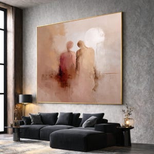 Könnte beinhalten: Großes abstraktes Gemälde mit goldenem Rahmen. Das Kunstwerk zeigt zwei Figuren in gedämpften Tönen von Rosa, Beige und Braun. Das Gemälde hängt über einem schwarzen Ecksofa in einem modernen Wohnzimmer.