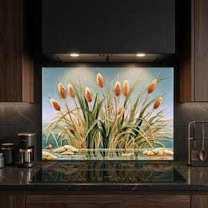 May include: A rectangular kitchen backsplash panel featuring a detailed illustration of brown cattails and green reeds growing near a calm body of water with light-colored stones at the base, set against a soft blue background.