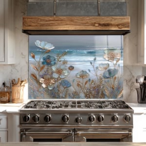 Puede incluir: Un protector de salpicaduras de cocina decorativo con una escena costera con flores azules y blancas y una vista del océano. La obra de arte está colocada sobre una estufa de gas de acero inoxidable.