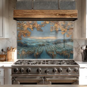 Puede incluir: Un protector contra salpicaduras de cocina de vidrio con un paisaje de viñedos con hileras de vides y colinas. La obra de arte tiene una paleta de colores azul y dorado, con una campana extractora de madera sobre una estufa de acero inoxidable.