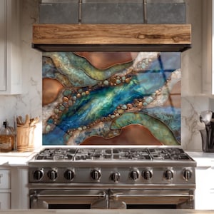 May include: A decorative kitchen backsplash with an abstract design. The artwork features a river-like pattern with shades of blue, green, and brown, resembling a flowing waterway. The backsplash is installed above a stainless steel gas range.